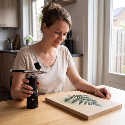 Vrouw aan de keukentafel met de airbrush en haar afgewerkte houten bord